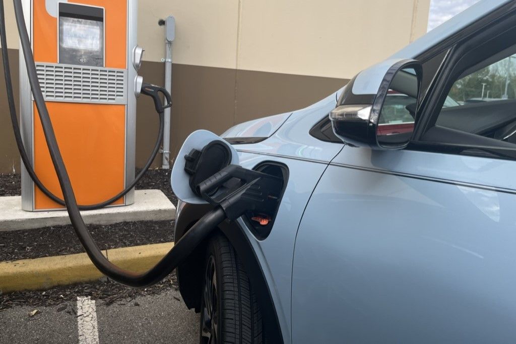 A blue electric vehicle charging at an orange charging station. 