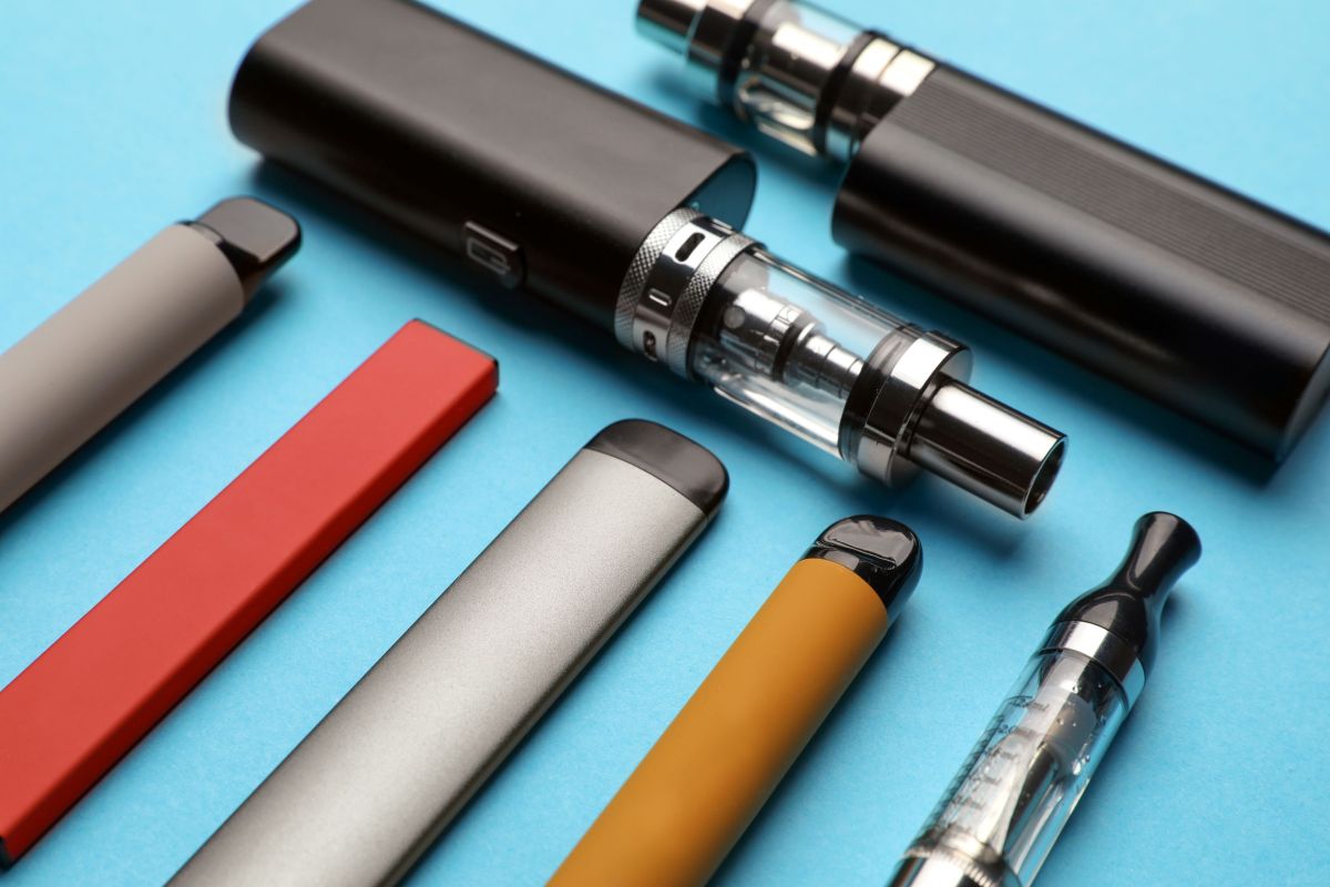 Different electronic cigarettes on light blue background, closeup