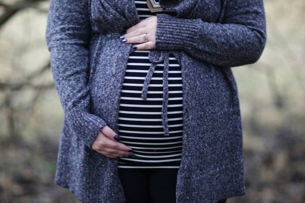 Pregnant woman wearing a sweater and holding her belly