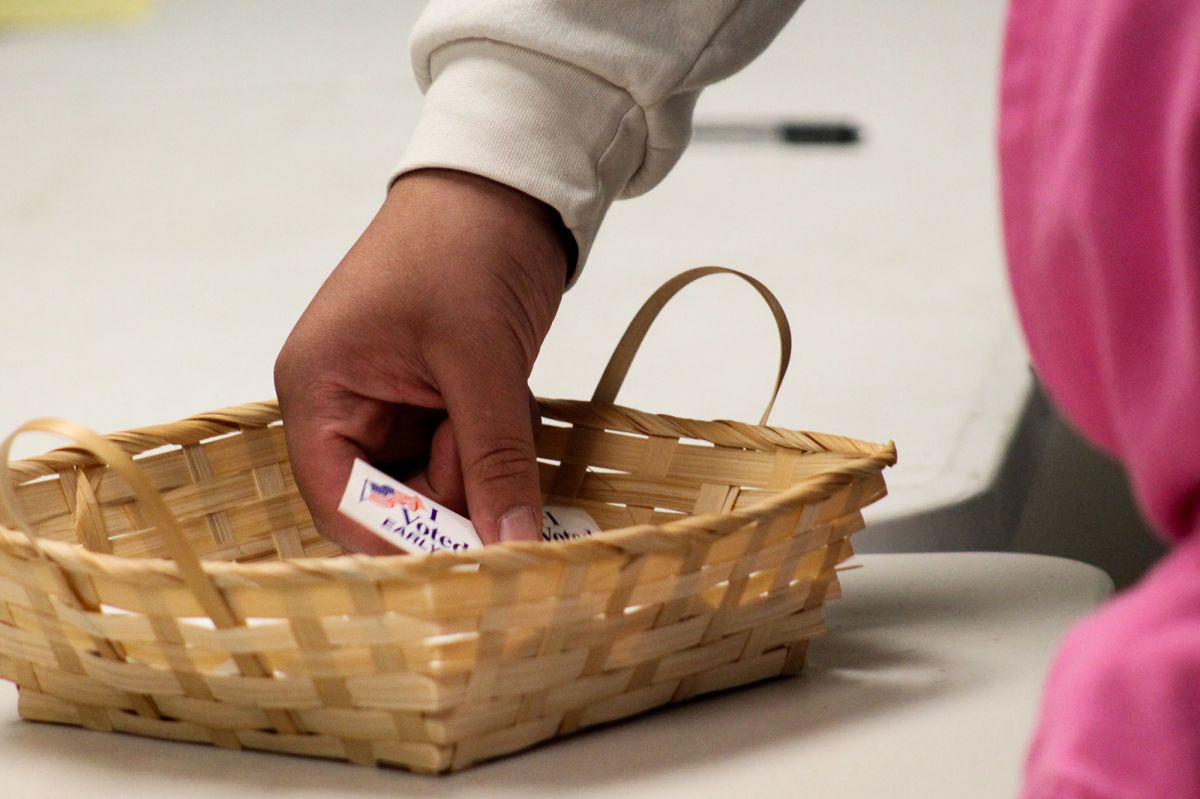 Stickers in a basket are picked through by a voter. The one visible says 'I voted early'