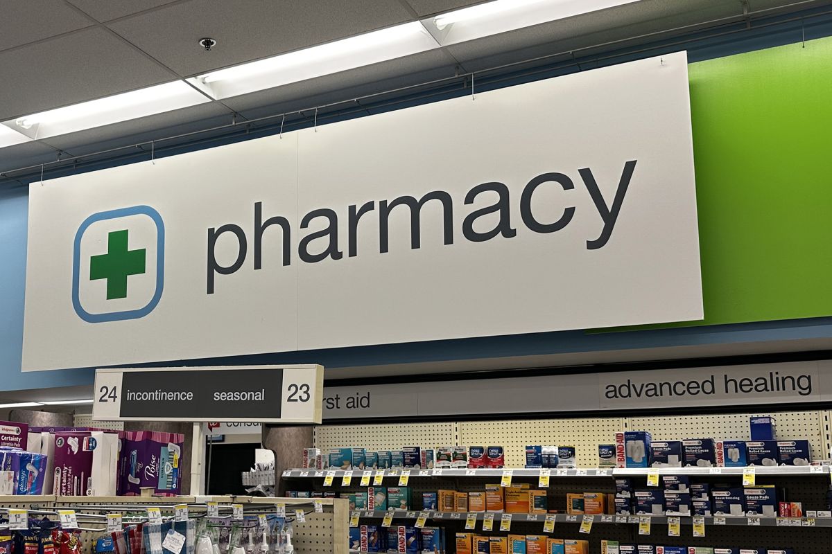 A sign hangs inside a store that says "pharmacy" in all lowercase letters in front of a light blue and lime green wall.