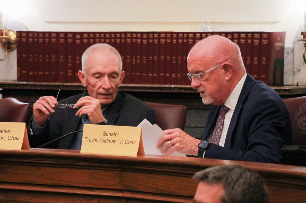 Jeff Thompson and Travis Holdman speak to each other while seated in a committee room