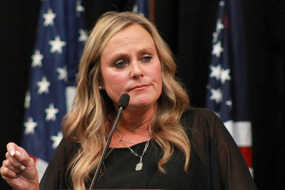 Jennifer McCormick speaks into a microphone on a stage with American flags standing behind her. 