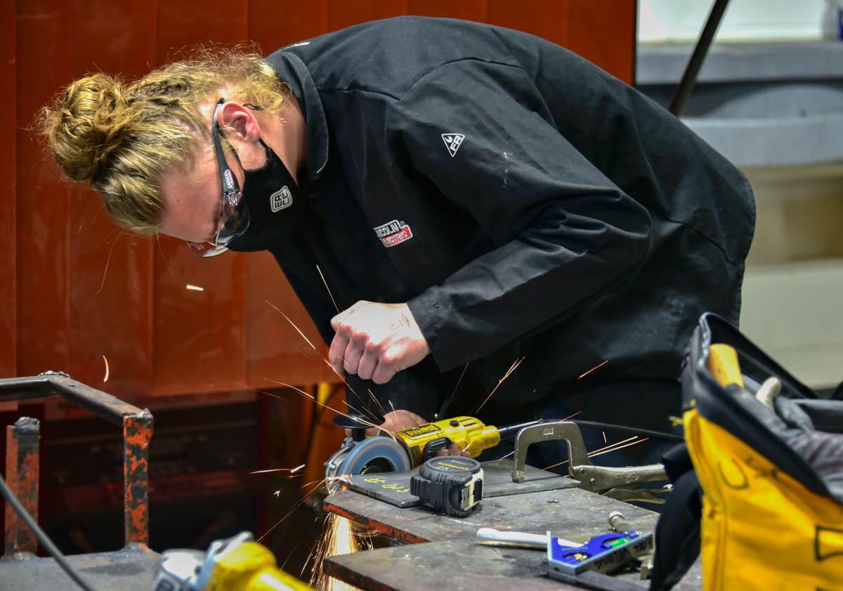 A young woman wears an all black outfit with a black mask. She has on clear safety goggles while she works on a project. 