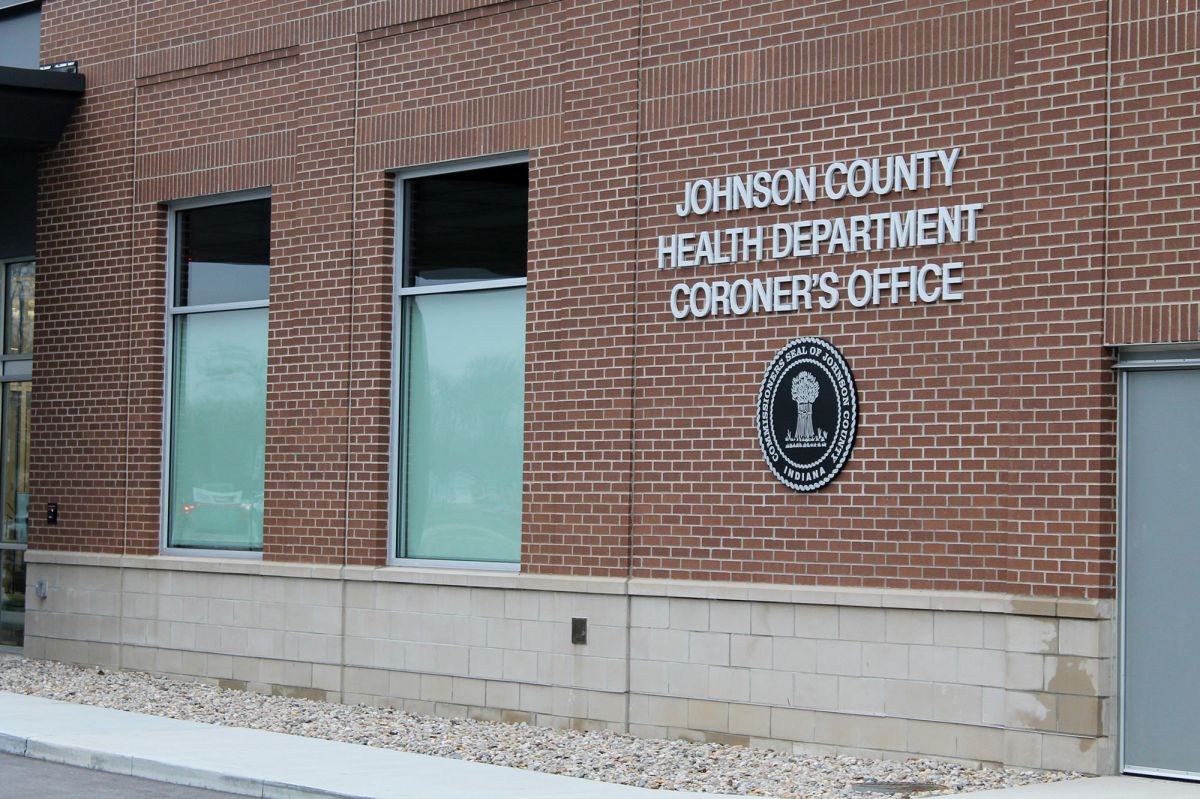 The sign for the Johnson County Health Department and Coroner's Office on the side of a brick building, with the county's seal underneath. 