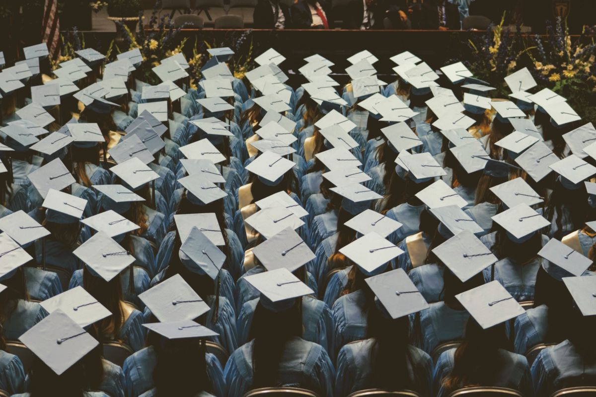 top-down view of the backs of rows of people at a graduation ceremony in blue cap and gown