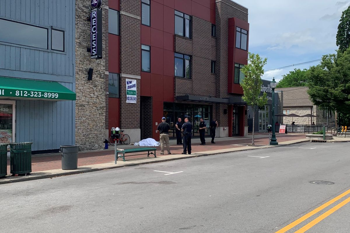 A photo of a man experiencing homeless dead with police officers surrounding.