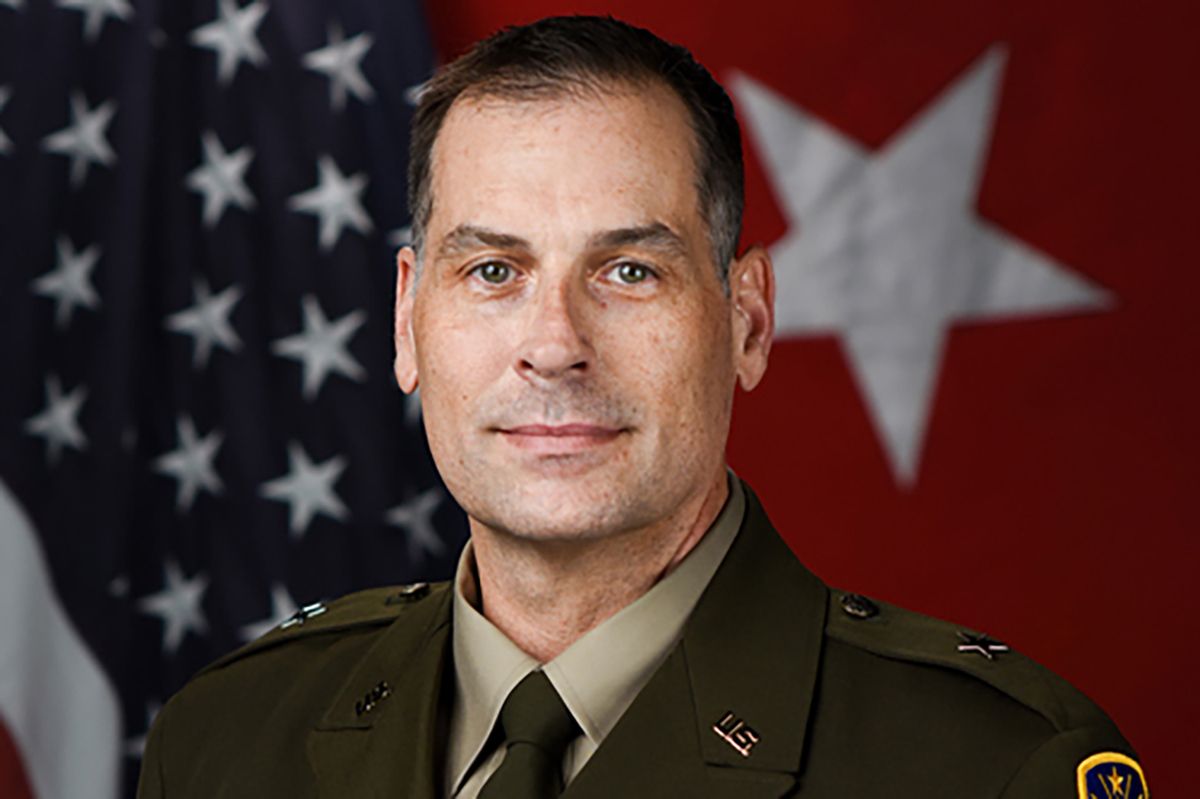 A portrait photograph of Larry Muennich. He is a White man with dark, slightly graying hair. He is standing in front of two flags and wearing his military uniform.