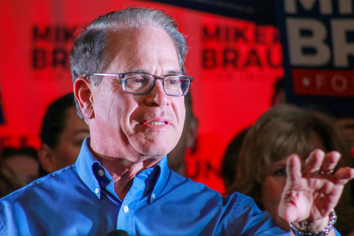 Mike Braun speaks to a crowd with supporters holding signs behind him.