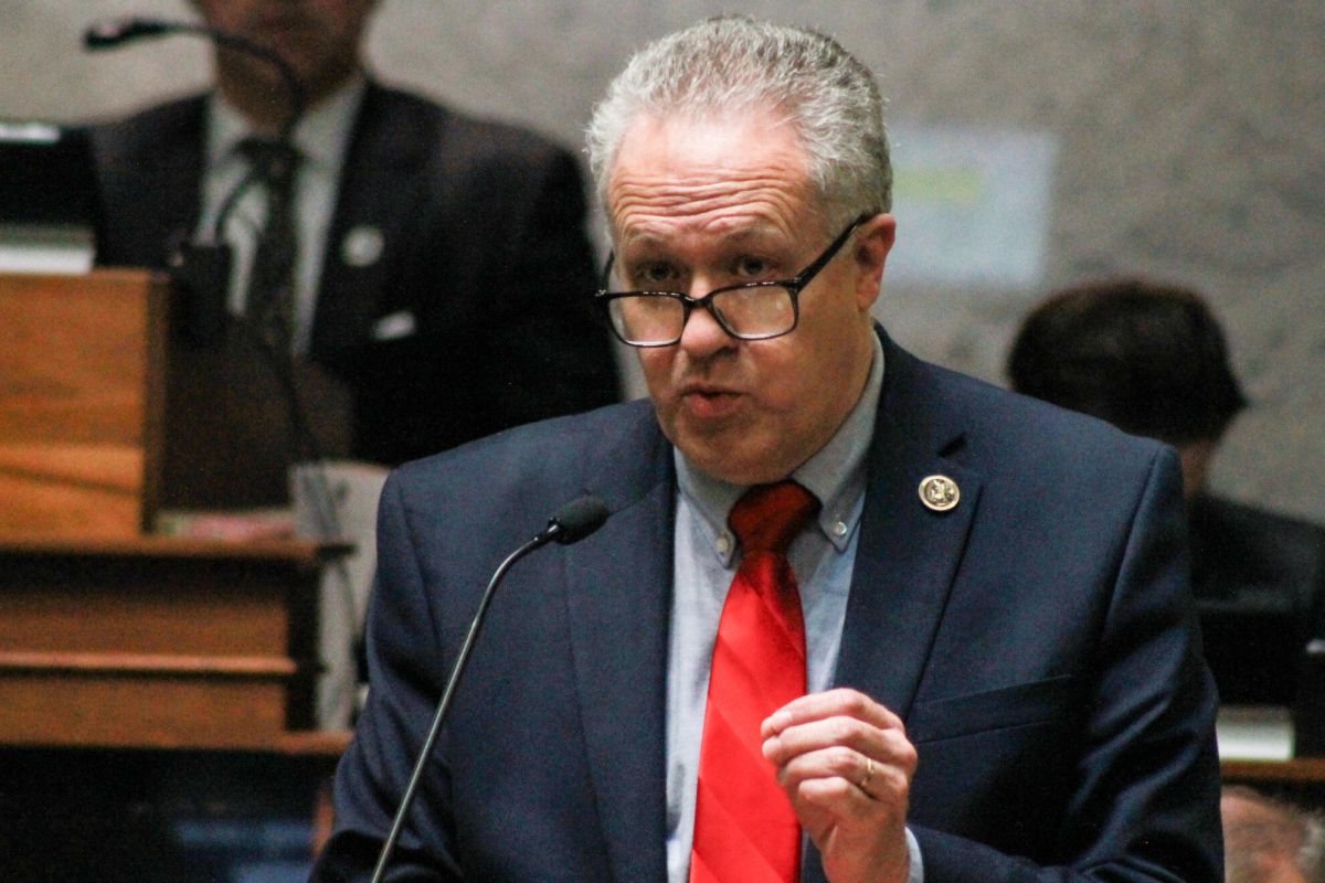 Mike Gaskill speaks on the Senate floor. Gaskill is a White man with white and gray hair. He is wearing glasses and a navy blue suit with red tie.