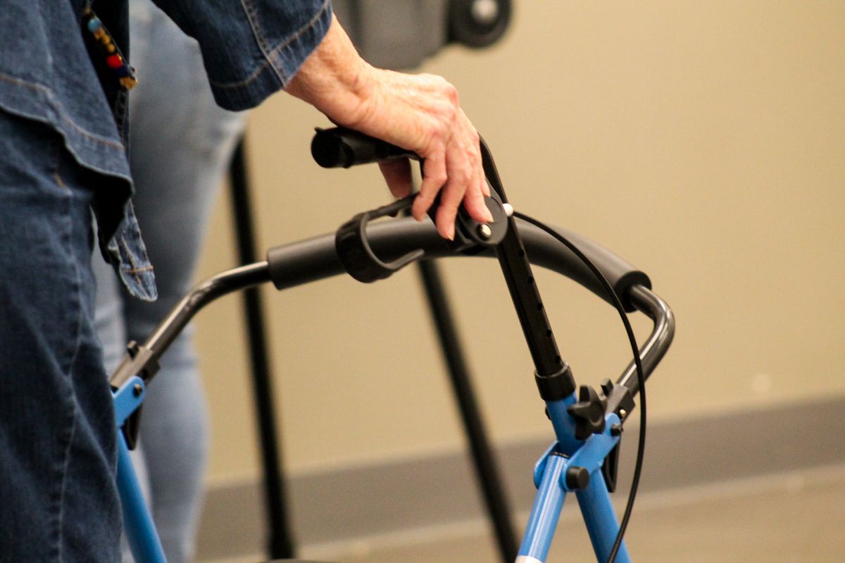 A older person in a jean jacket and jeans uses a walker as a mobility aid.