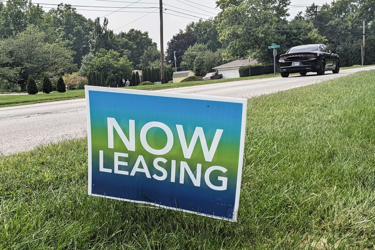 A Now Leasing sign is posted in a lawn in front of an apartment complex.