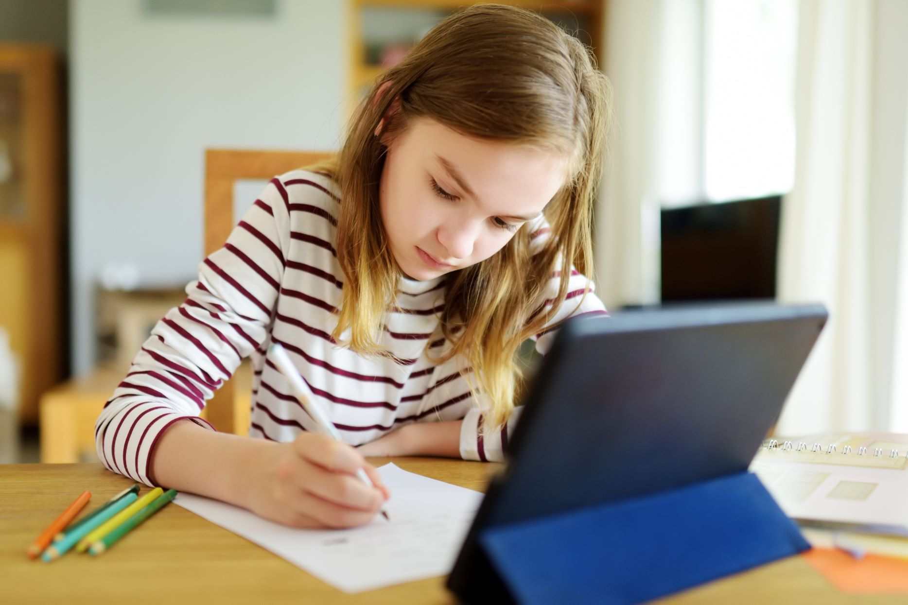 Smart preteen schoolgirl doing her homework with digital tablet at home. Education and distance learning for kids. Homeschooling during quarantine.