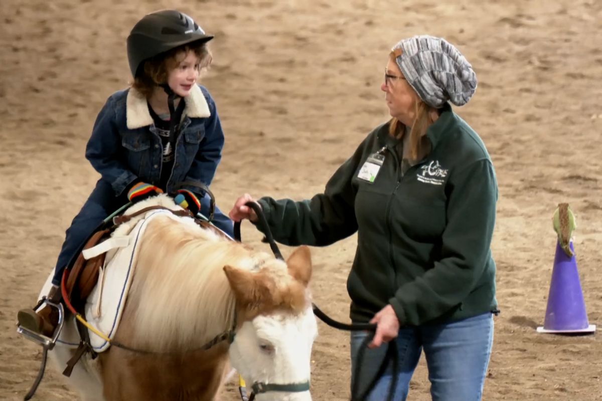 A volunteer at the PALS Adaptive Riding Center leads a young girl on a horse.