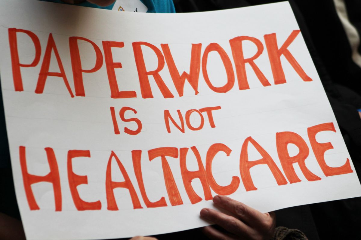 A sign that reads "Paperwork is not healthcare" in bright orange text.