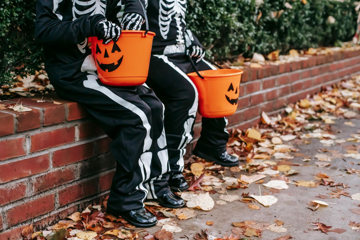 hildren in Halloween costumes resting on fence with jack o lantern buckets