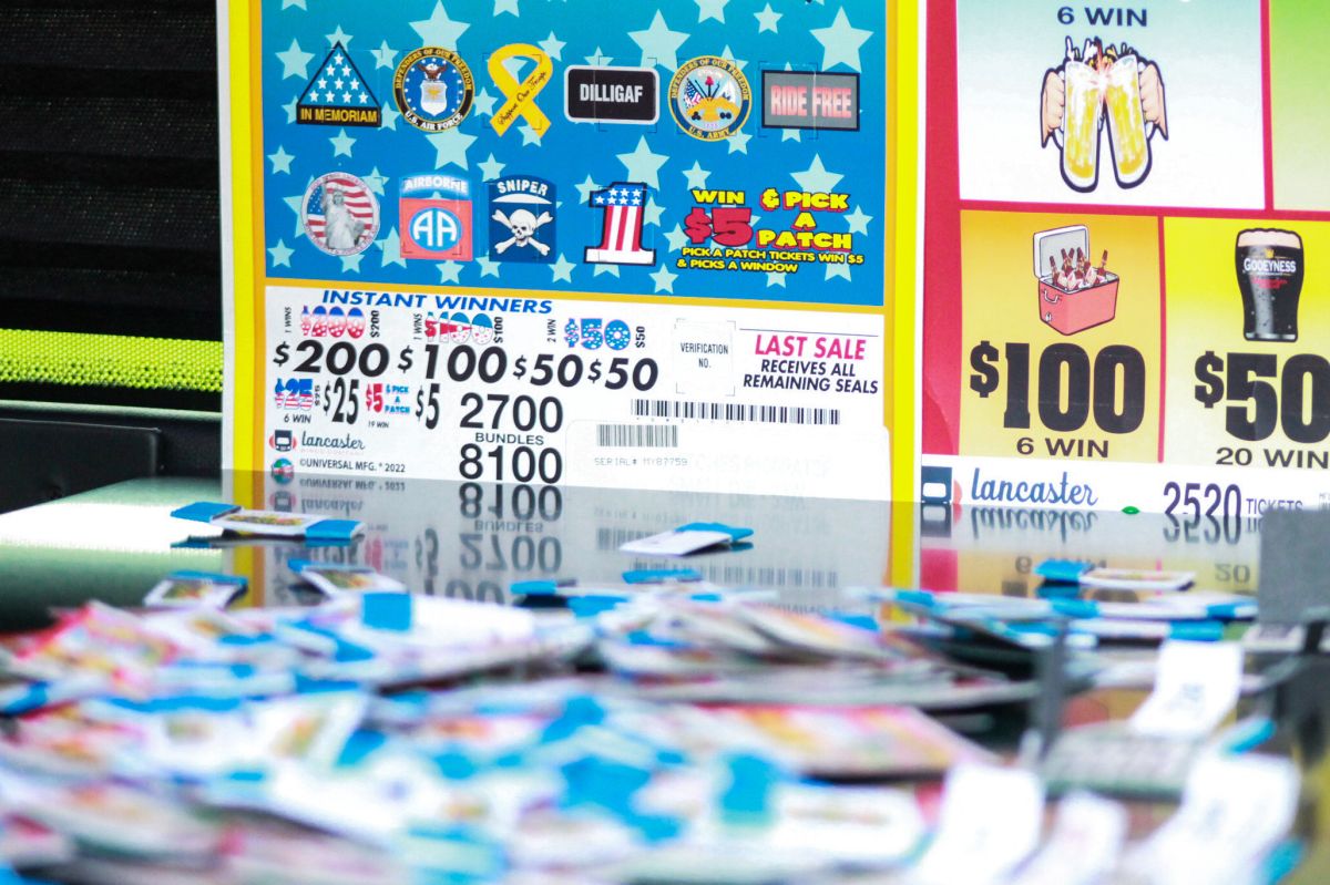 Strips of multi-colored paper are strewn across a table top in the foreground, out of focus. In the background are signs displaying prize amounts for pull tab charity games.