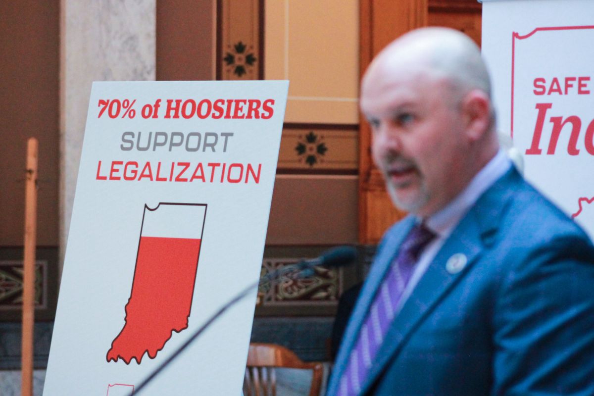 A poster on an easel reads "70 percent of Hoosiers support legalization." Heath VanNatter is in the foreground of the image, out of focus.