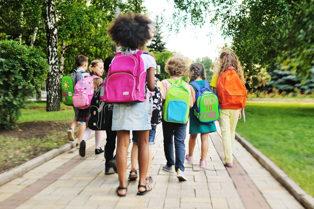 A group of children with backpacks walking on the sidewalk.