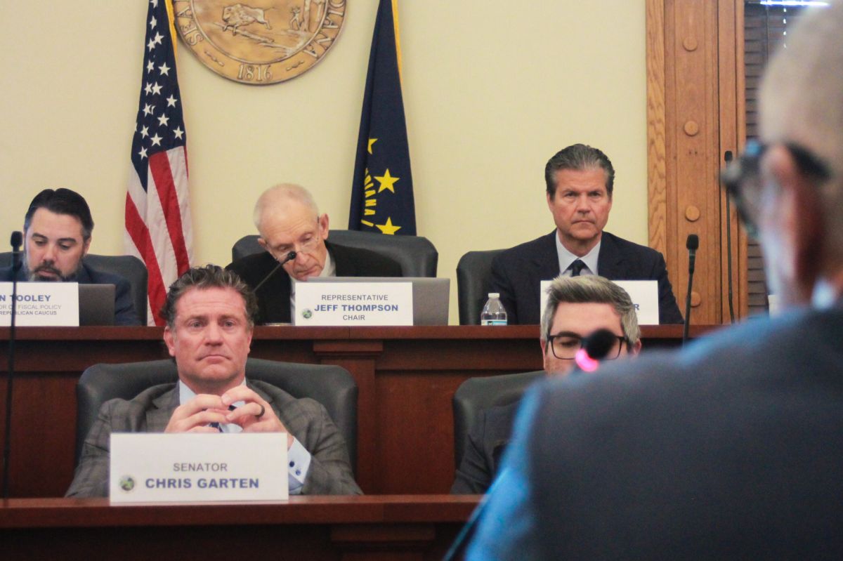 Lawmakers sit in their chairs on two tiers of desks, watching someone speak to them.