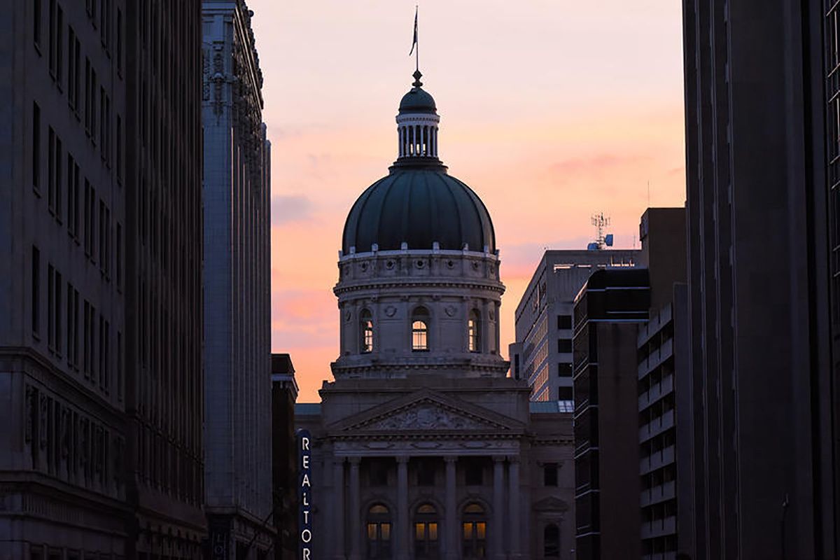 The Statehouse, at sunset, framed by buildings downtown.