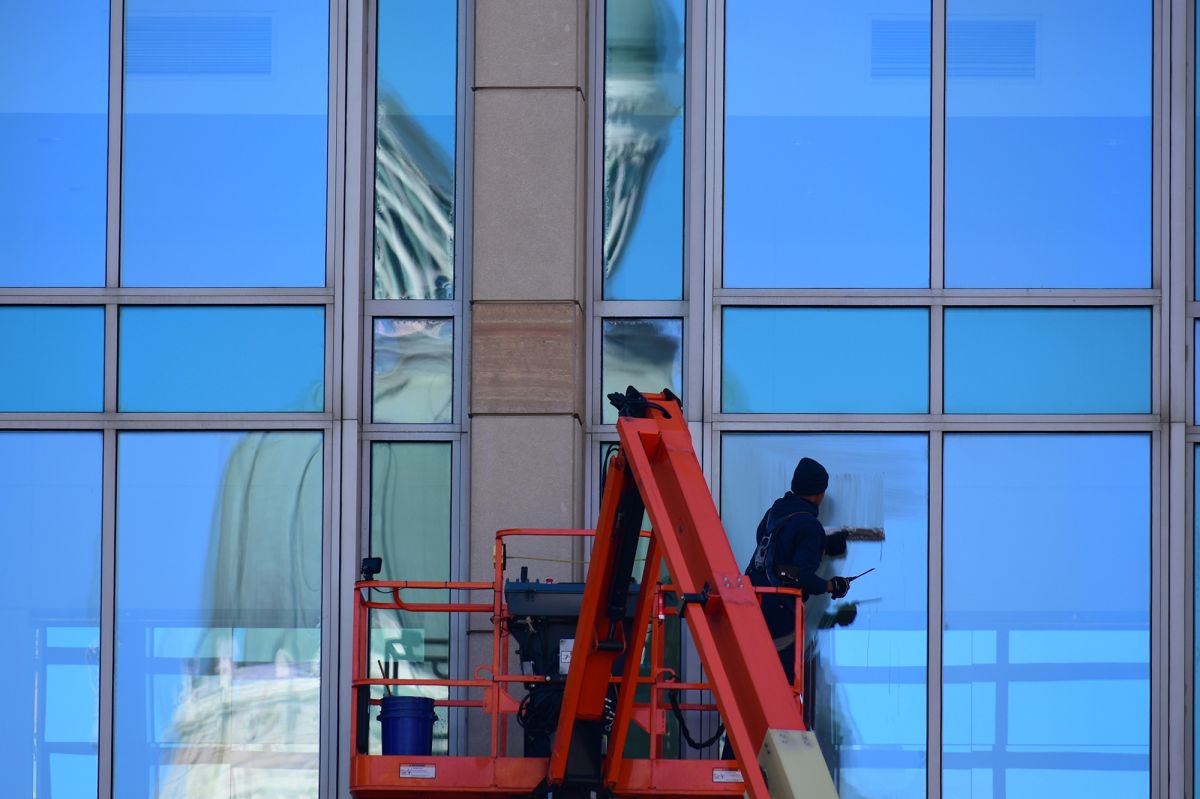 A window washer works on a building across the street from the Indiana Statehouse. You can see the Statehouse reflected on the windows.