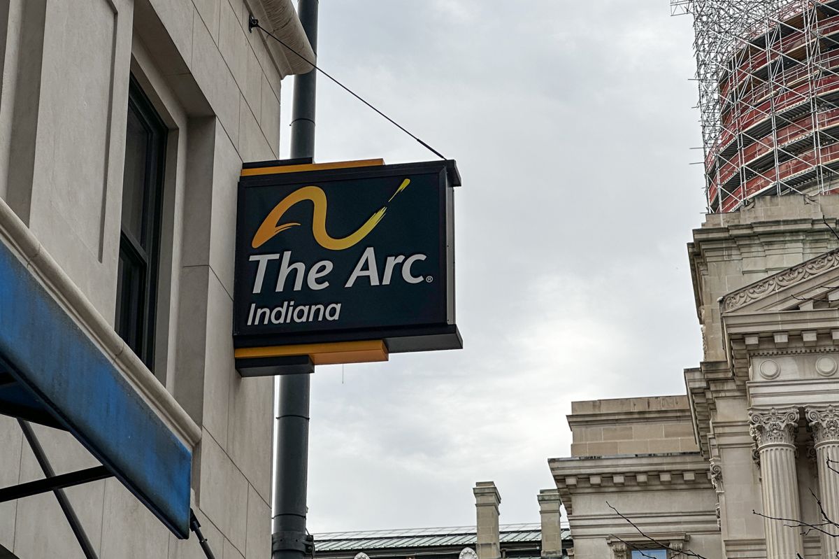 A sign for The Arc of Indiana on the side of a building with the Indiana Statehouse in the background. 