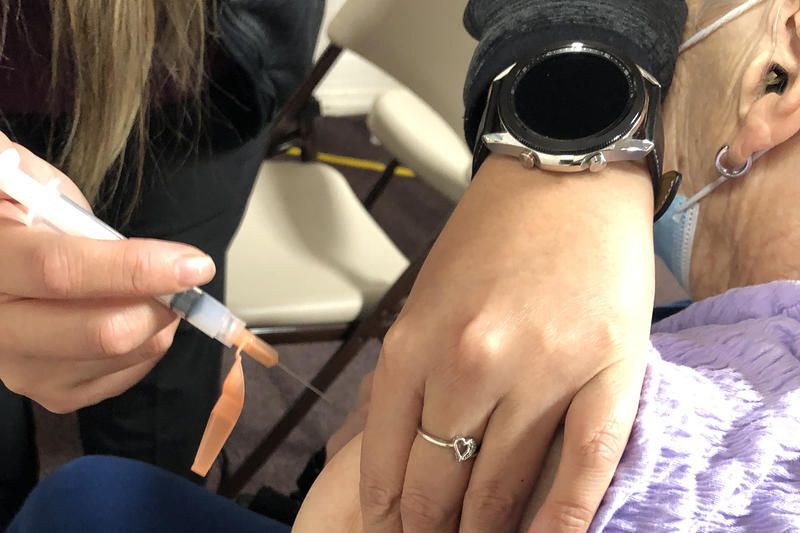 A health care provider delivering a vaccine via syringe into someone's arm. 