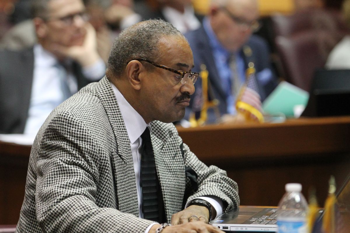 Vernon Smith is a Black man, wearing a checked suit. He has short grey hair and a mustache. 