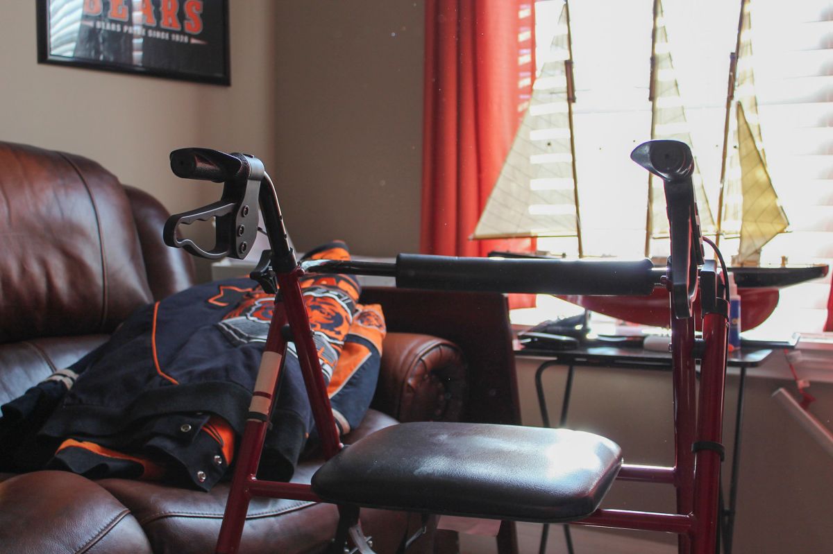 A walker sits in front of a leather couch with a Chicago Bears jacket on it.