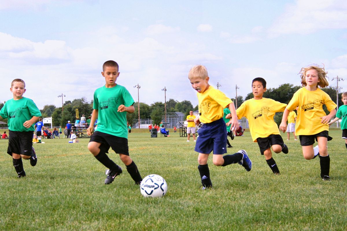 Children in green and yellow shirts run and kick a soccer ball.