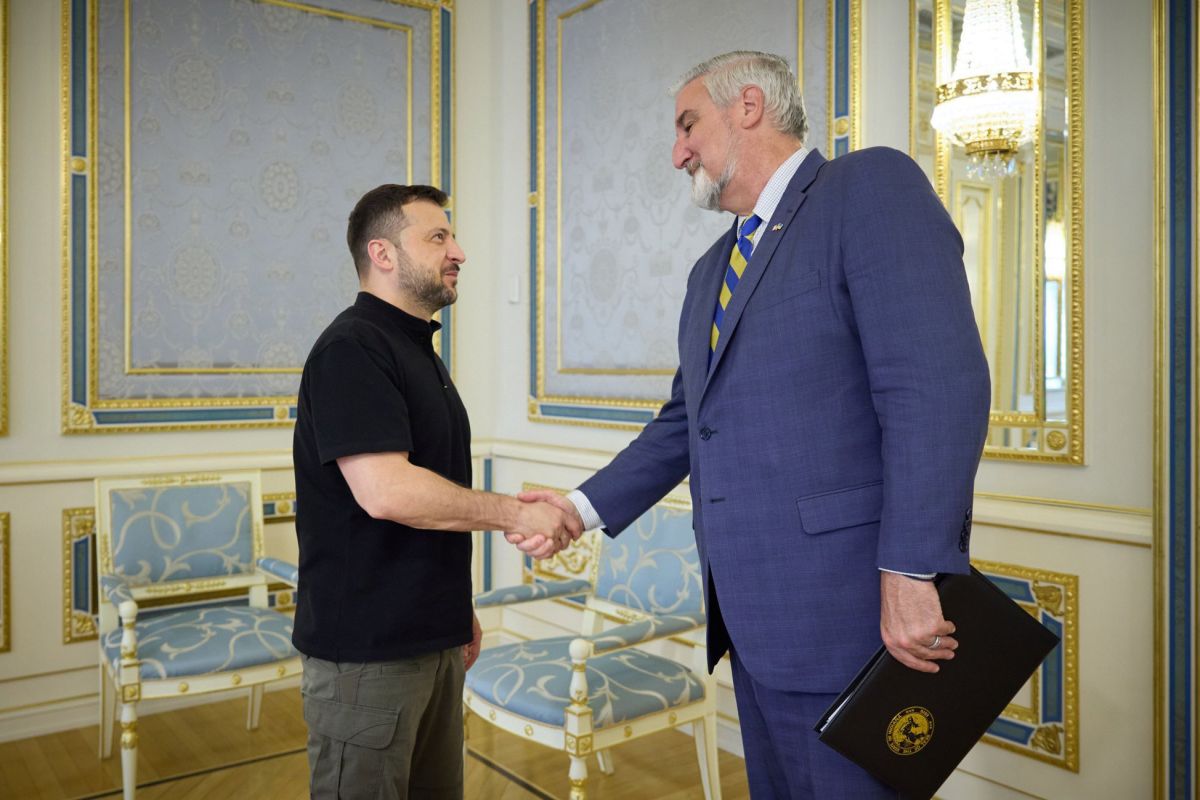 Eric Holcomb is a White man with white and gray hair and beard. He shakes hands with Ukrainian President Volodymyr Zelenskyy, who has dark hair and a short beard.