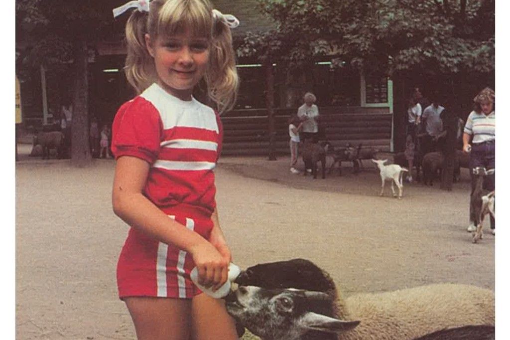 Young girl with pony tails feeding baby sheep with a bottle.