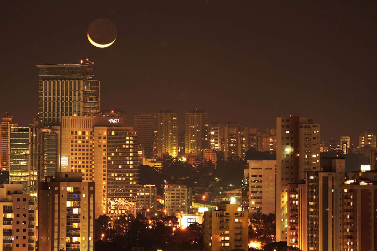 The moon shines over a brightly lit city
