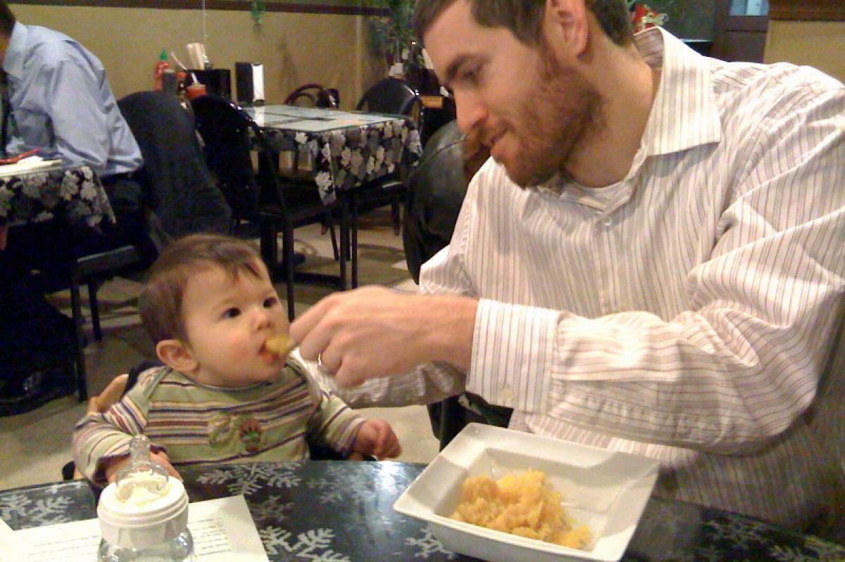 man feeding baby with here comes the airplane