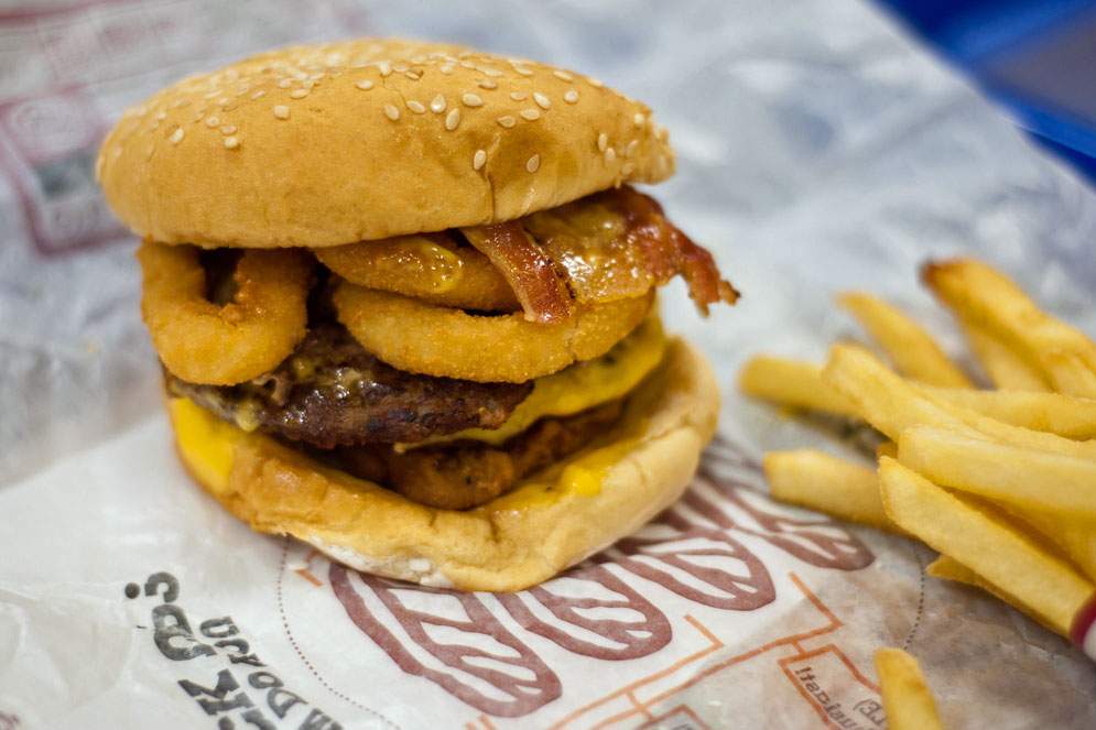 burger with bacon and onion rings with fries on wax paper