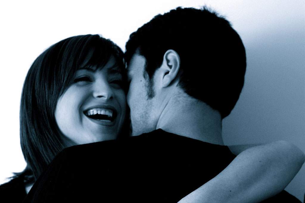 woman smiling while hugging a man in black and white