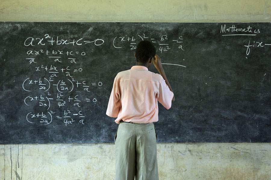 boy standing at chalkboard doing mathematics