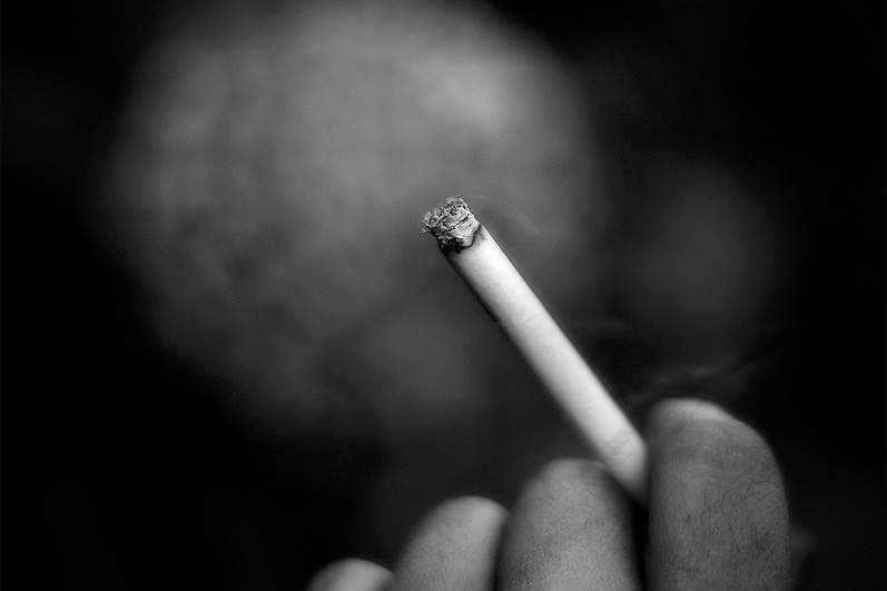 black and white photo of someone holding a smoking cigarette in their hand