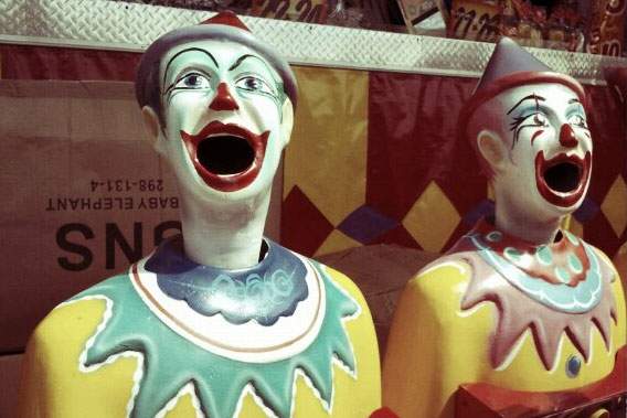 Two busts of laughing clowns are displayed in a carnival booth.