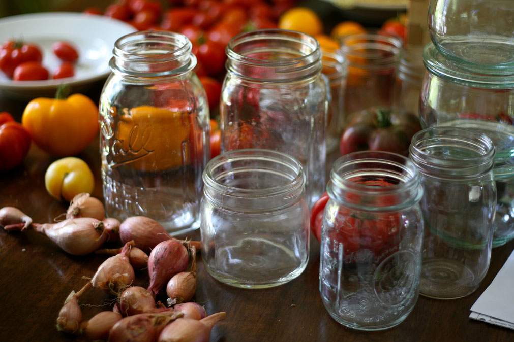 Glass mason jars are displayed next to garden vegetables in preparations for canning season.