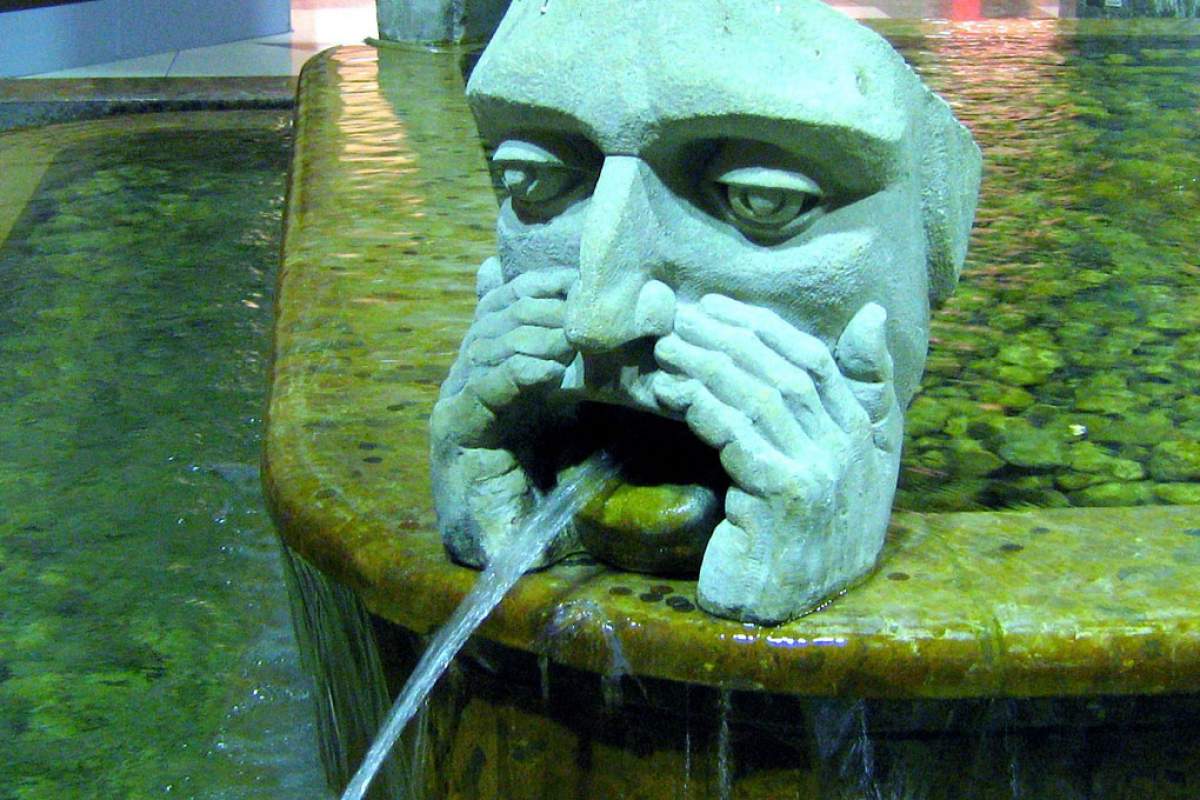 A water fountain shoots a stream of water from a human face.