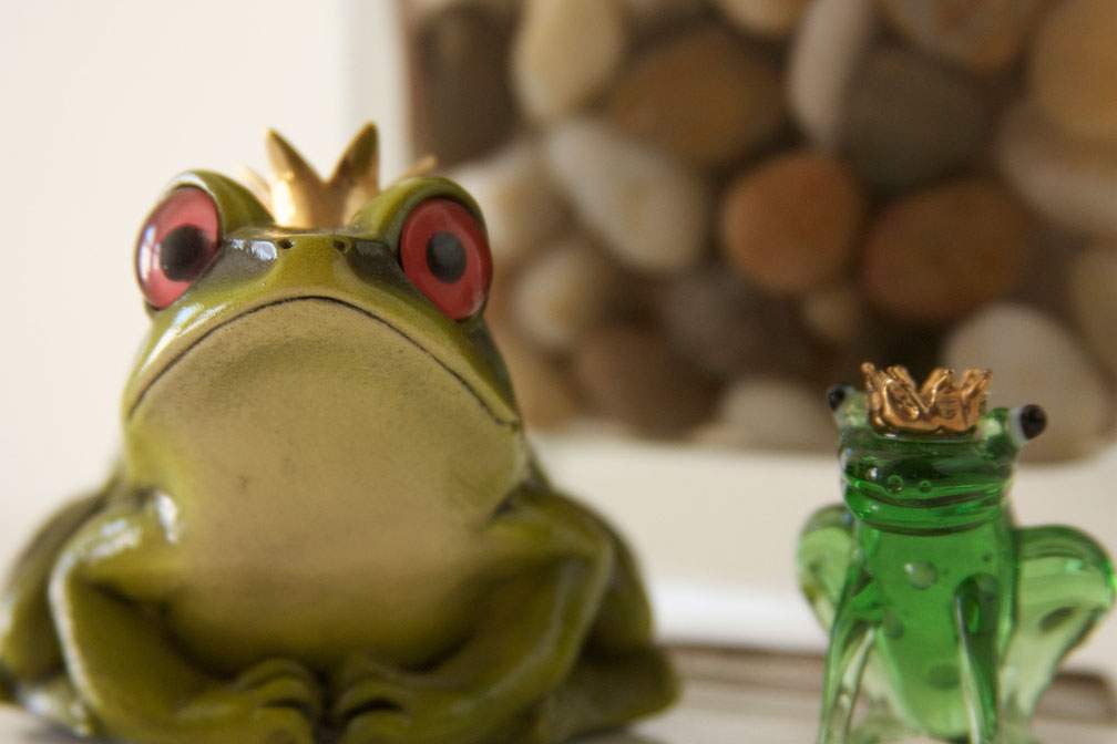 A large frog adorned with a crown poses near a smaller frog adorned with a crown.