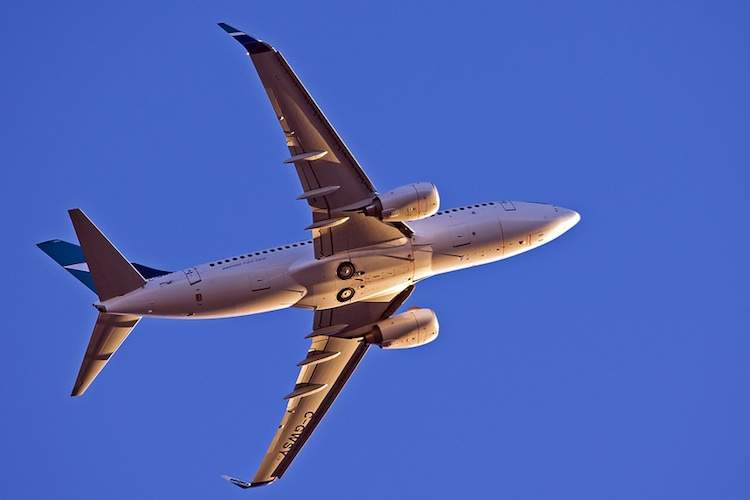 The underside of a commercial airliner taking off at sunset