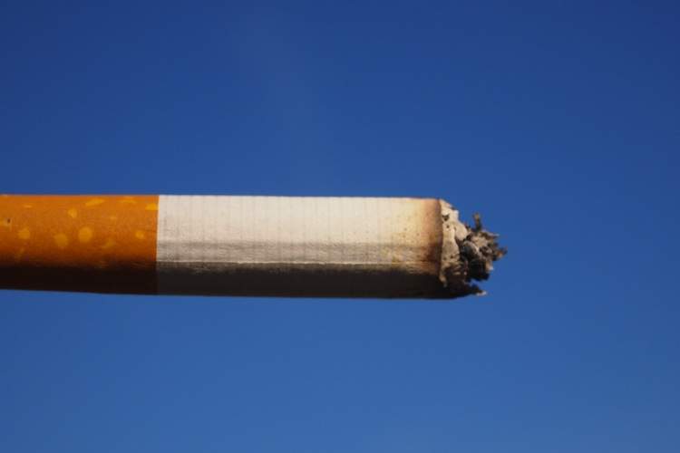 A cigarette burns against blue sky