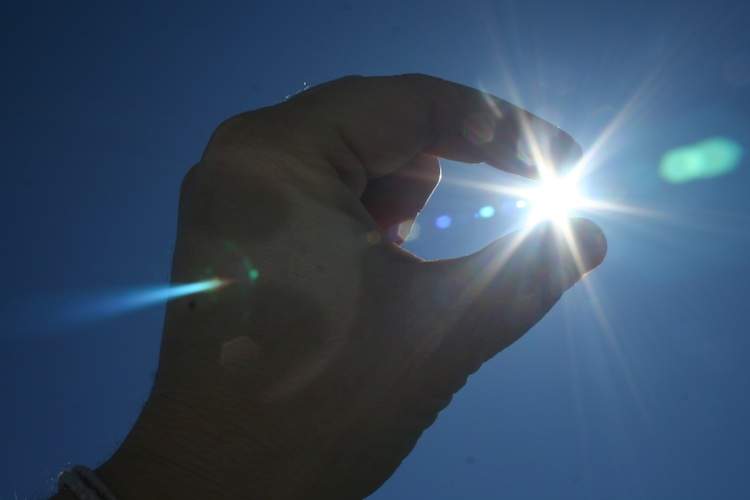 Fingers appear to pinch the sun