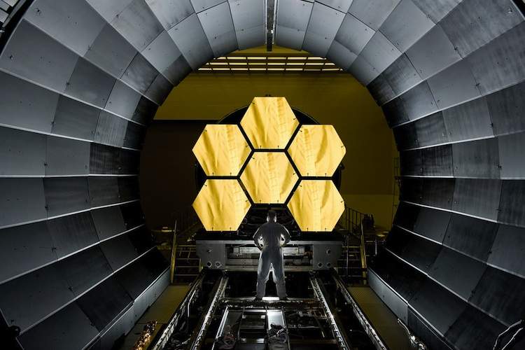 A technician stands in front of six of the James Webb Telescope's gigantic mirrors.