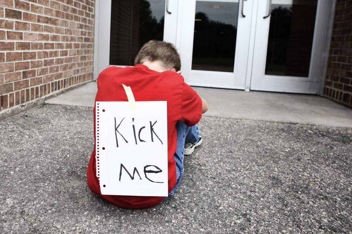 child with "Kick Me" sign