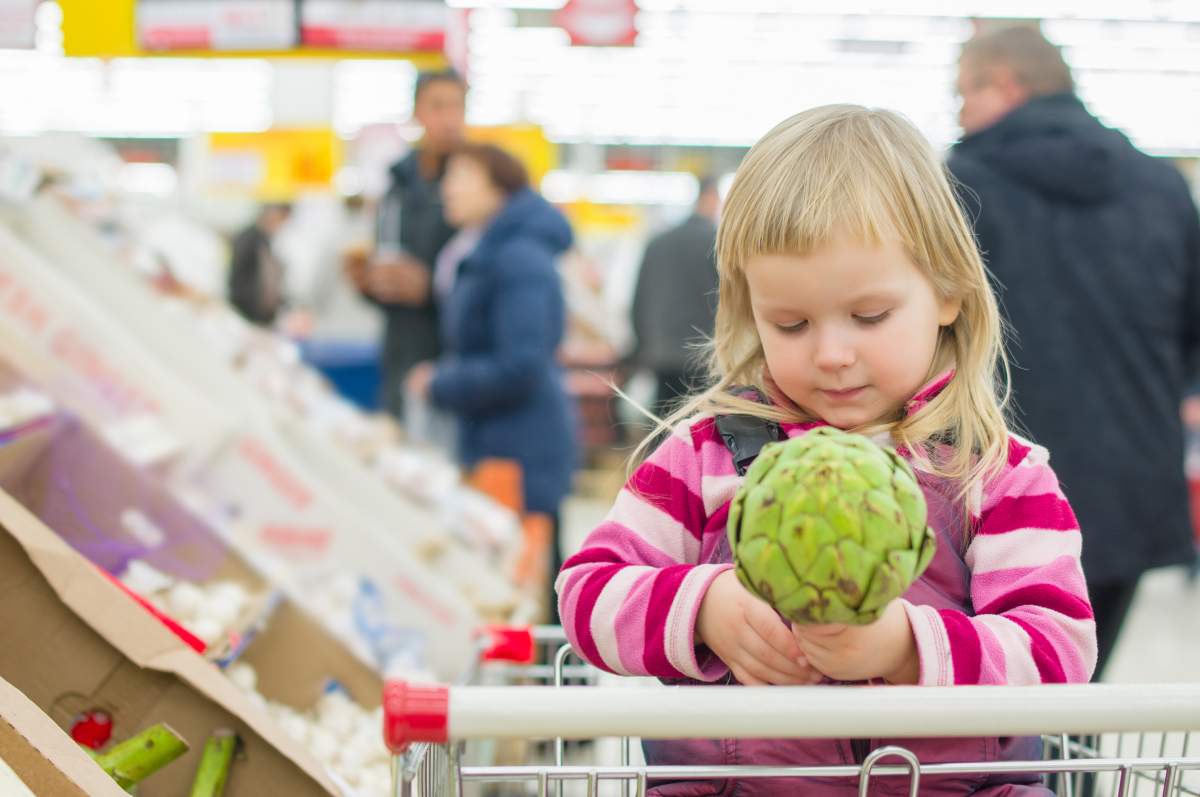 kid in a grocery cart holds an artichoke