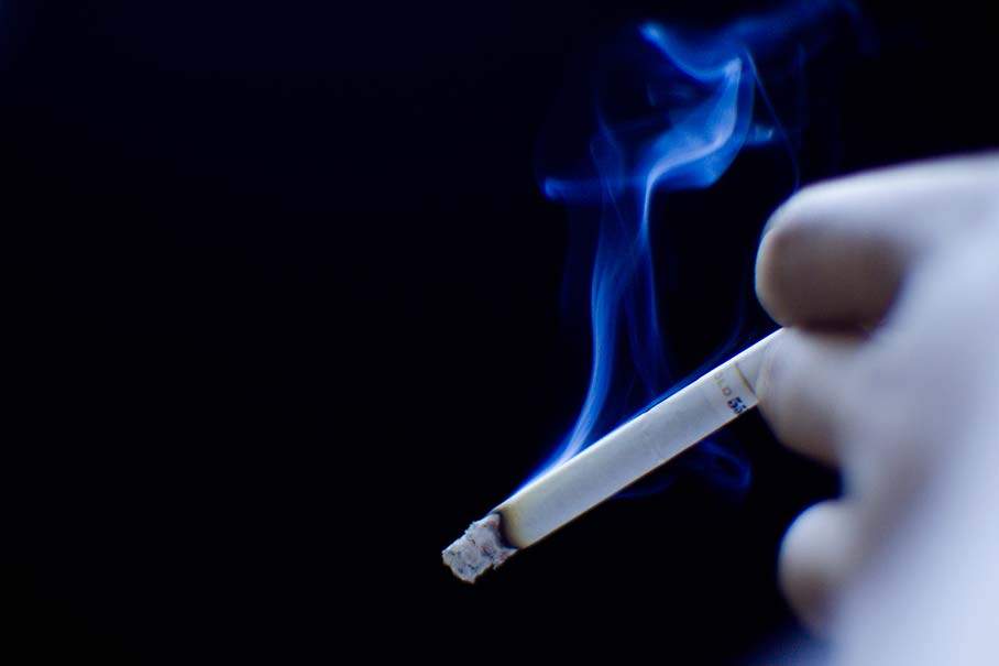 hand with lit cigarette and plume of smoke
